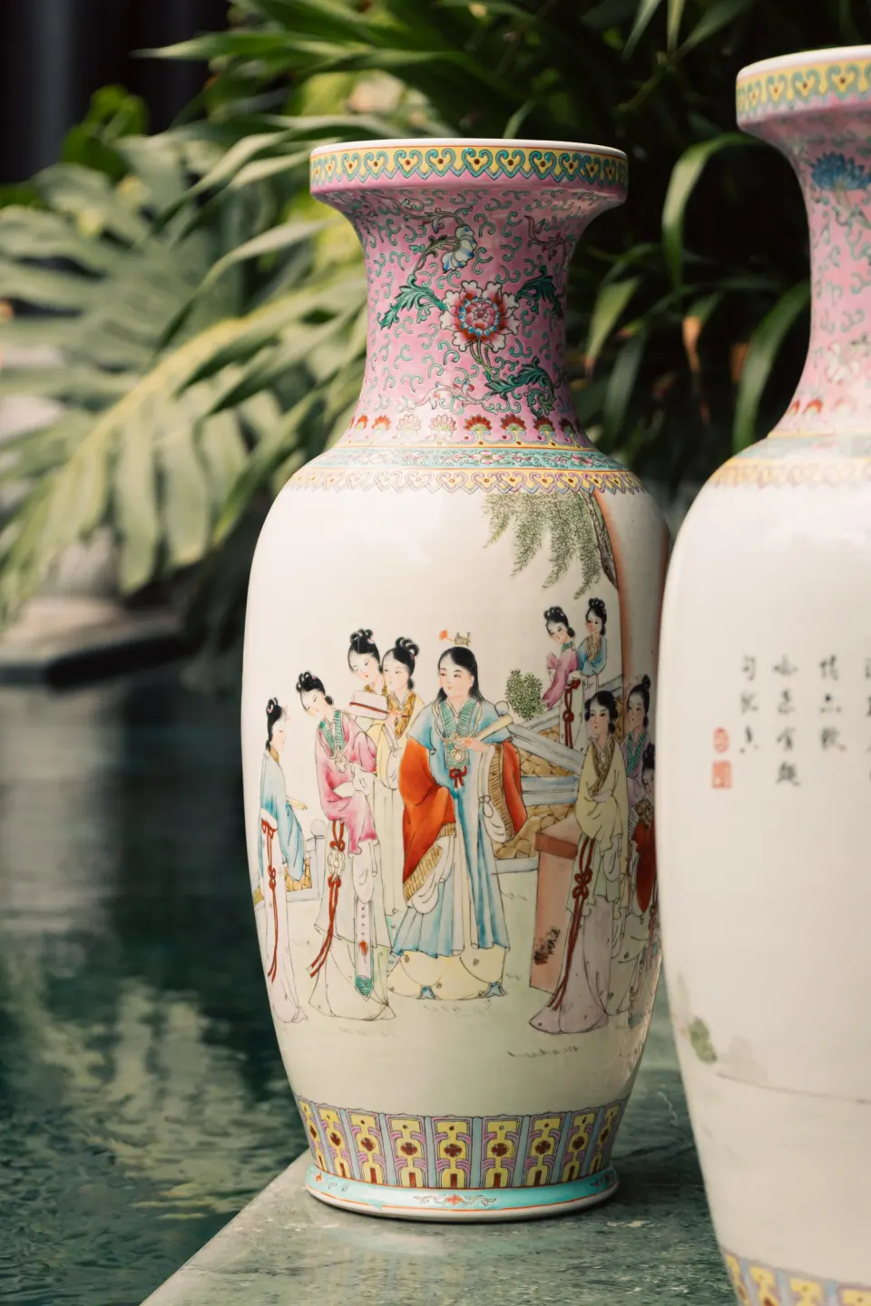 Two tall painted vases with figures among monstera leaves.
