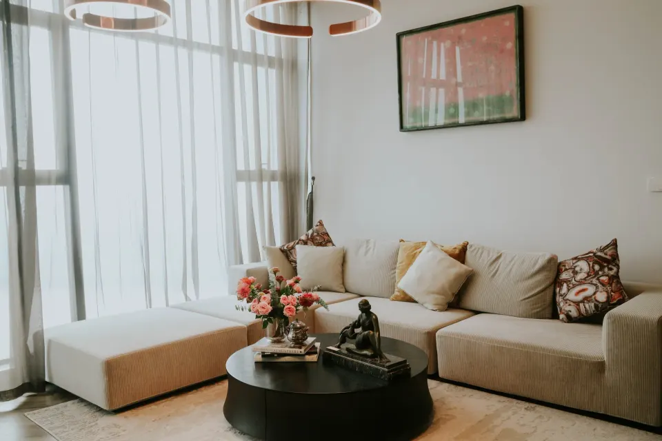 A bright living room with a pink-and-green painting, a cream sofa and a bouquet on a round table.