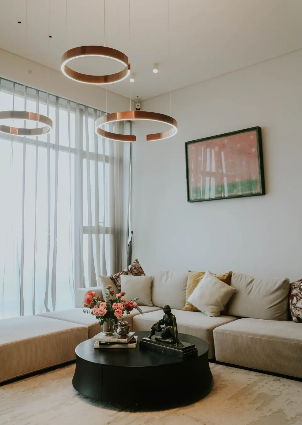A living room with copper ring lights, a cream sofa and a pink painting.
