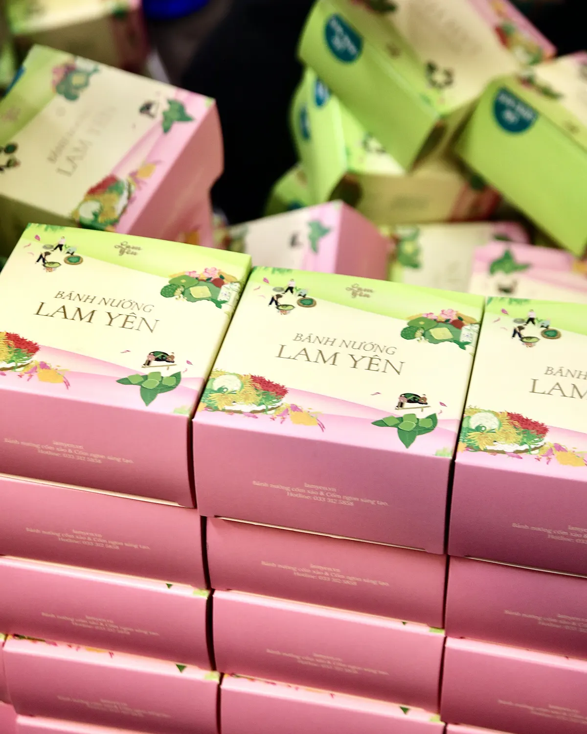Stacks of pink gift boxes lettered “Bánh Nướng Lam Yên”, with green and pink boxes piled up behind them.