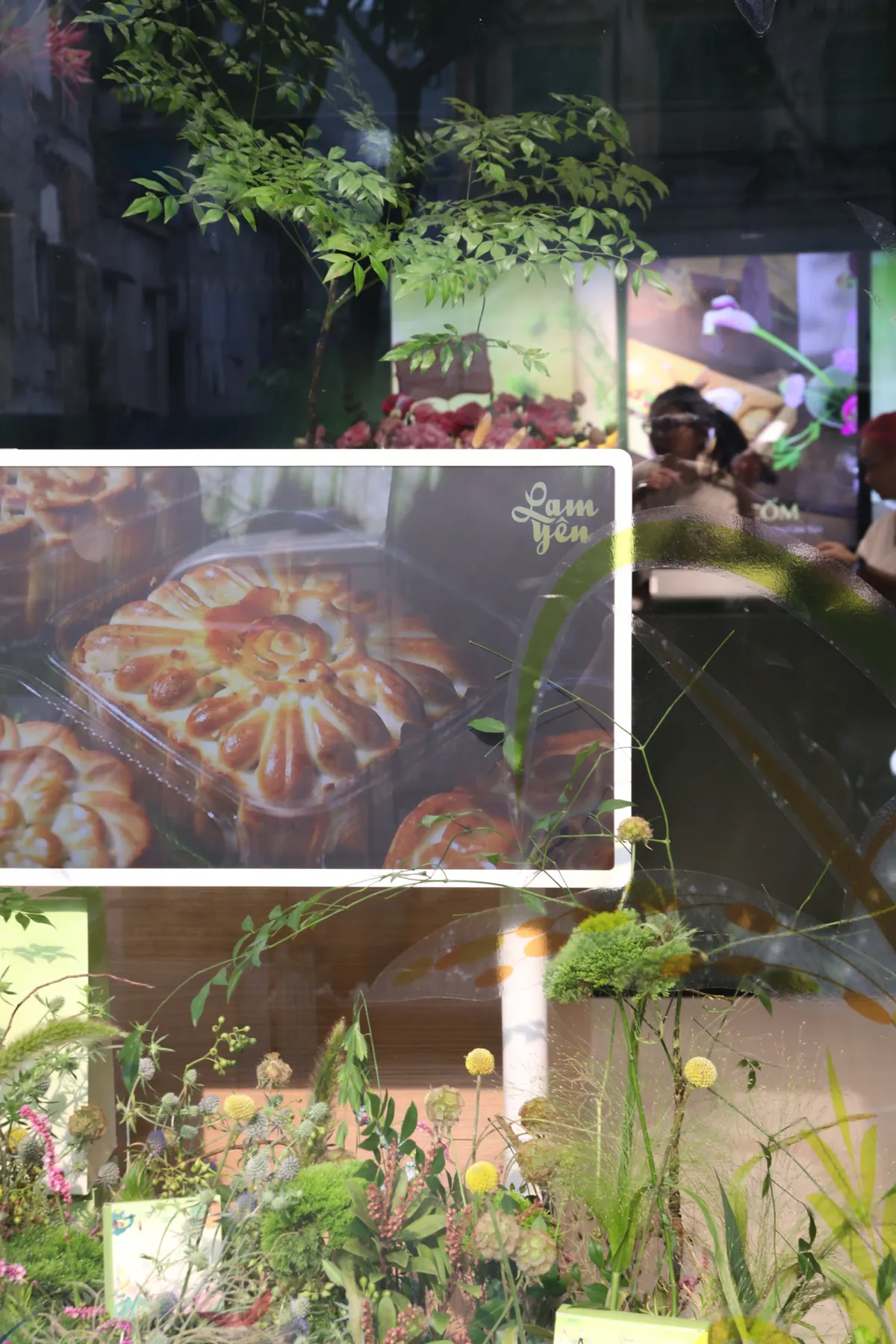 Plants and flowers in the shop window, with a framed photo of baked mooncakes.