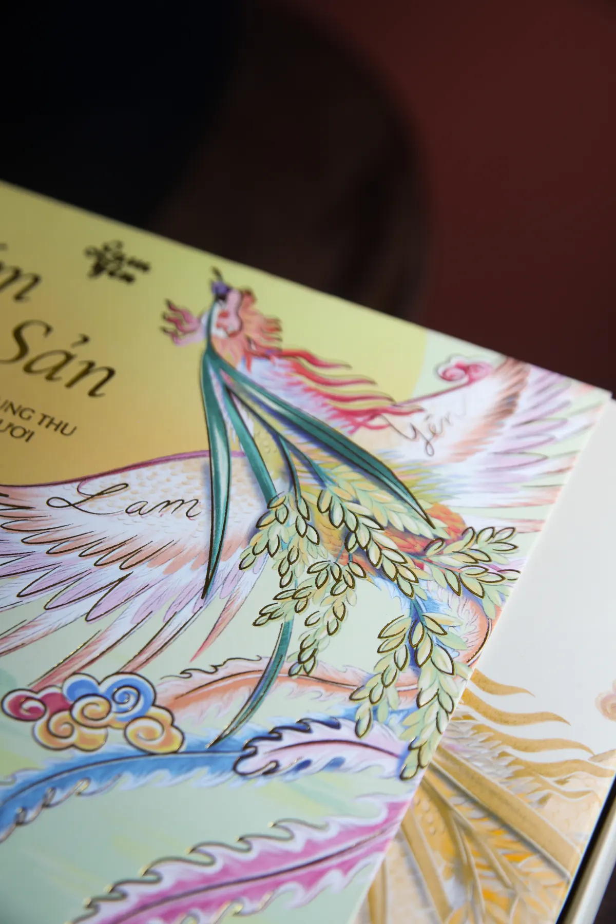 Close-up of the Cốm Đặc Sản box: a phoenix with outspread pastel wings among clouds.
