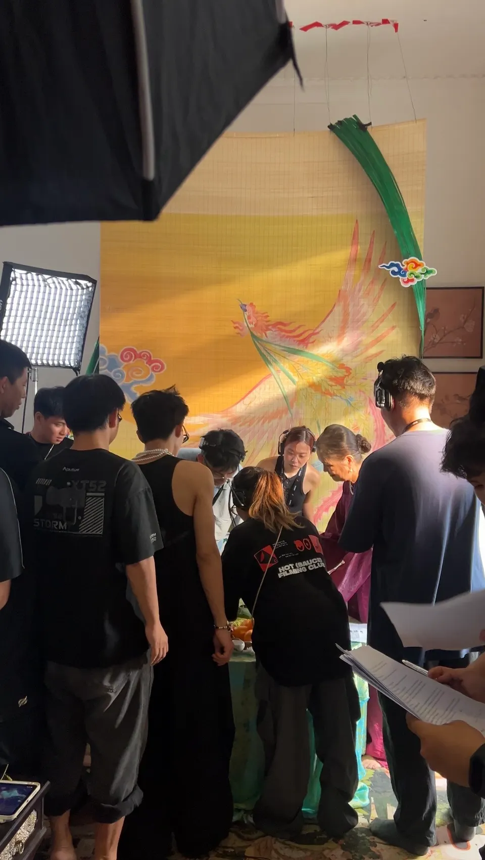 The crew gathered around a set with a yellow painted backdrop and a softbox light.