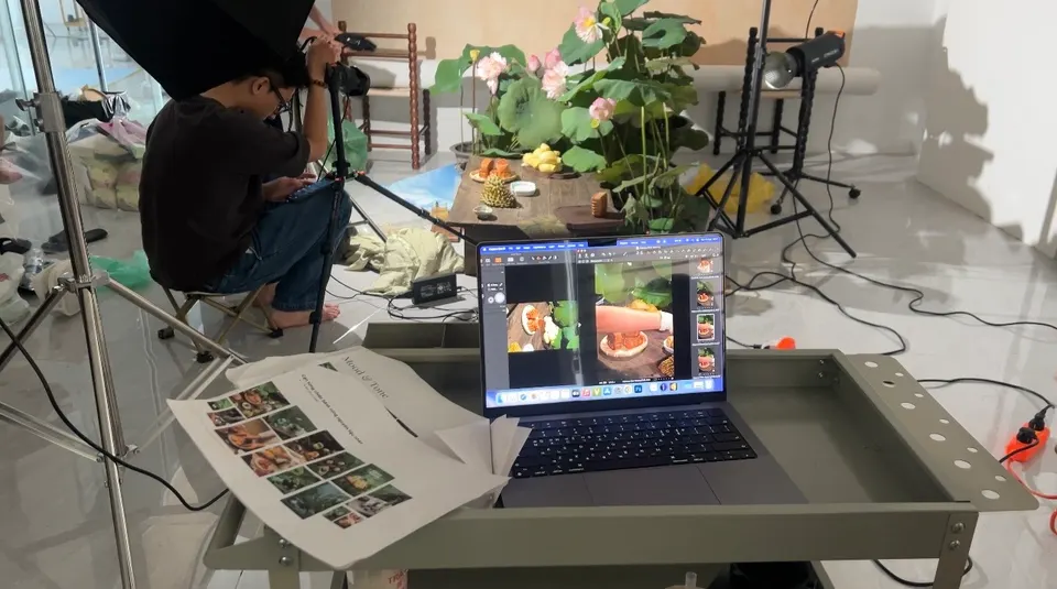 A laptop on a tray showing photos, a printed contact sheet beside it, and a camera operator behind.