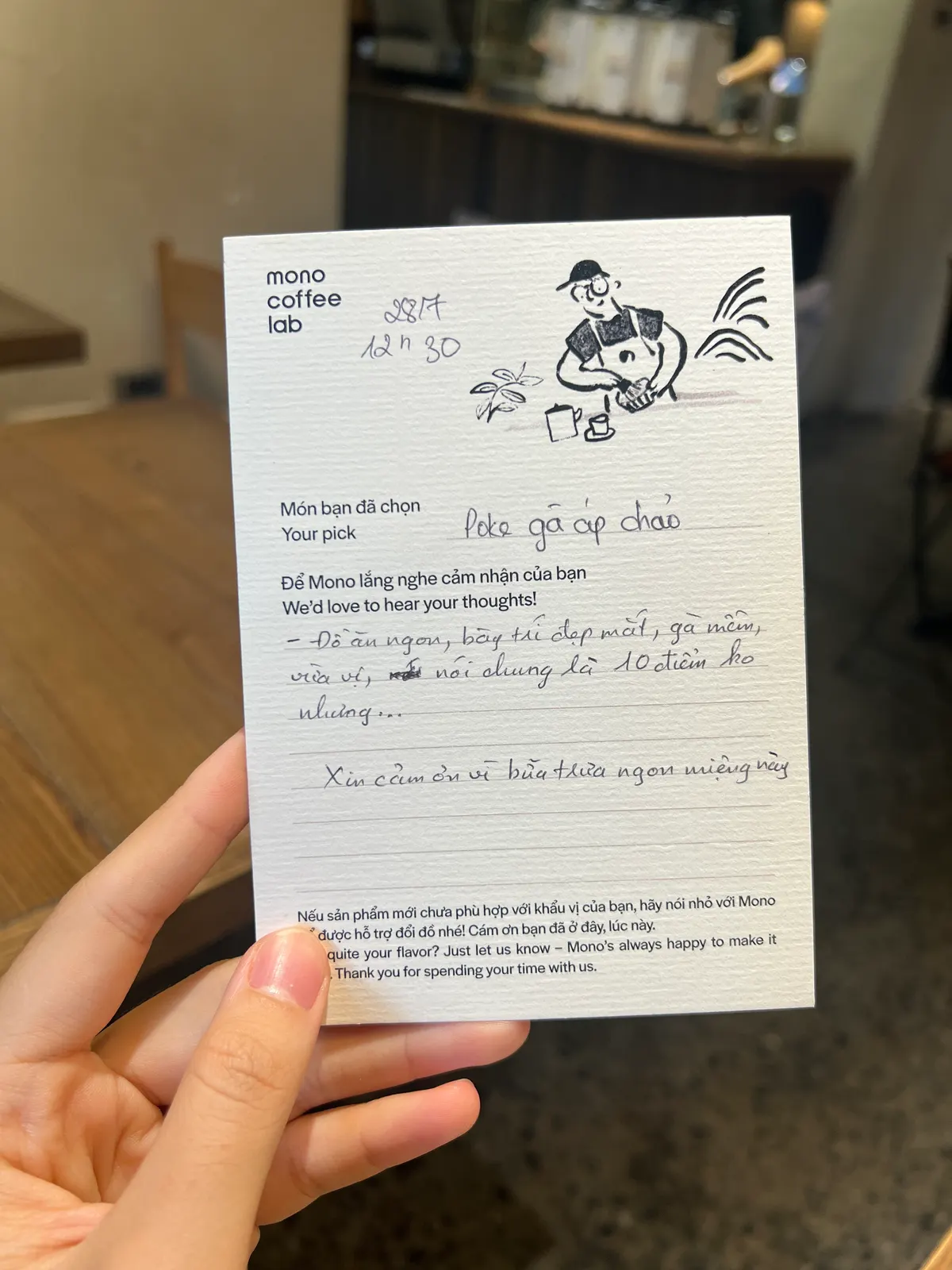 A hand holding up a Mono Coffee Lab guest opinion card, filled in by hand, in the café (card 2 of 9).