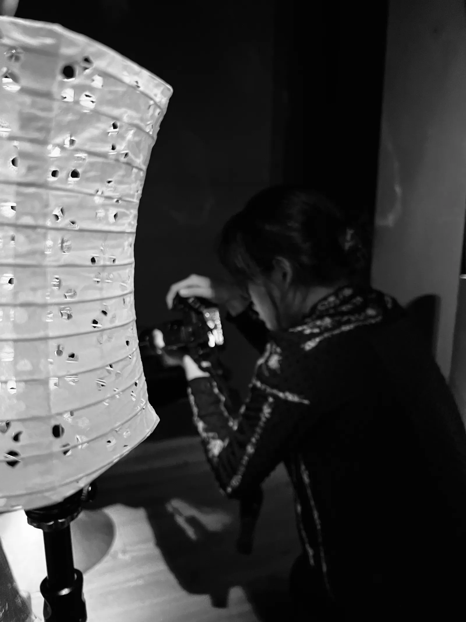 Black-and-white photo of Cam Anh crouching to shoot beside a tall lantern pierced with small holes.