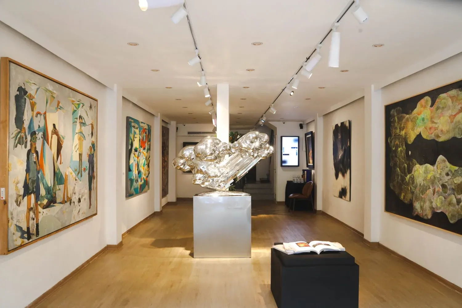 The long white gallery hall with large paintings on both walls and a silver sculpture at the end.