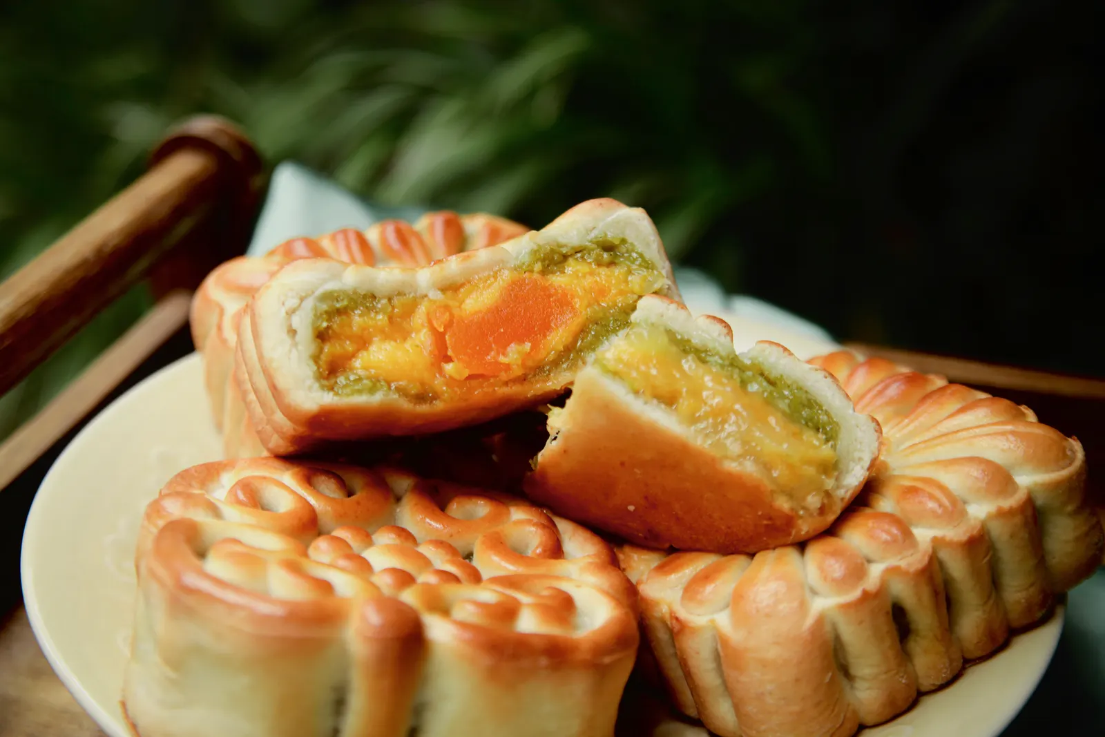 Baked mooncakes on a pale plate, one broken open to show a golden egg-yolk and green cốm filling.
