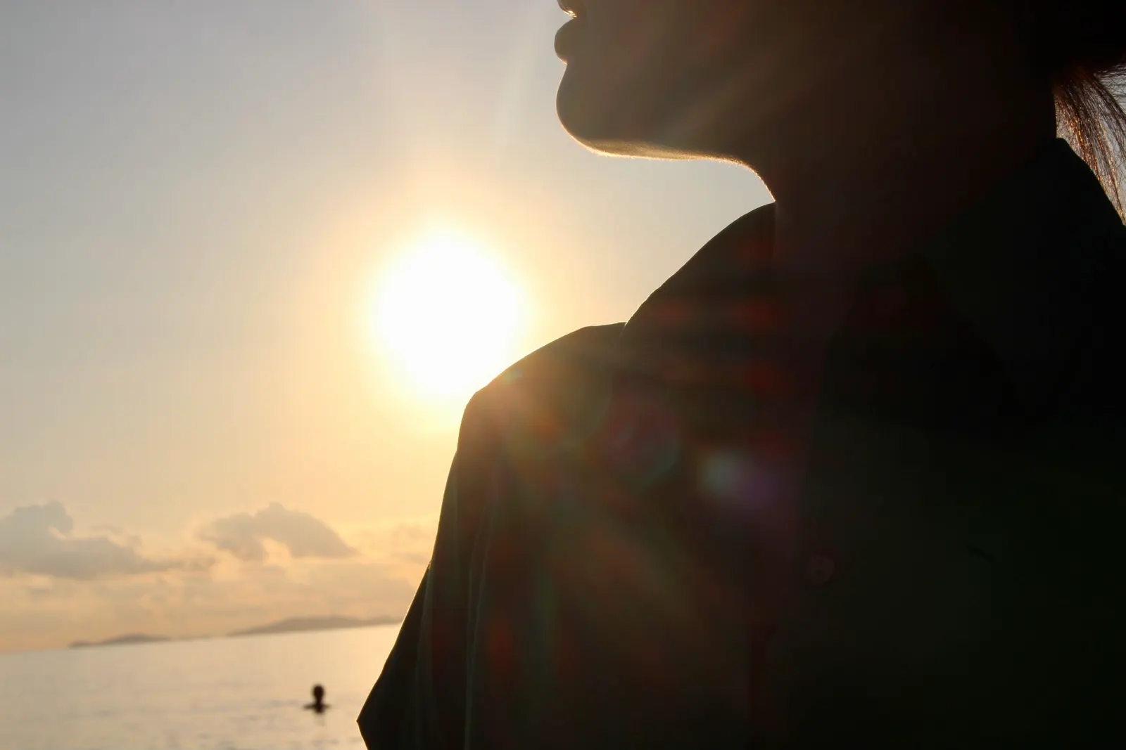 The profile of Cam Anh’s face and shoulder in silhouette against a low golden sun over the sea.